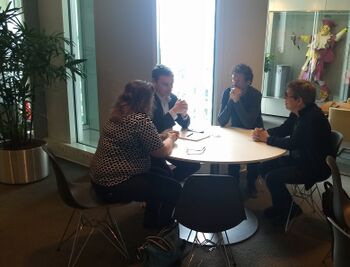 Foto van een viertal pratende mensen aan een tafeltje, de individuele deelnemers zijn onherkenbaar gemaakt in verband met privacyregulering.